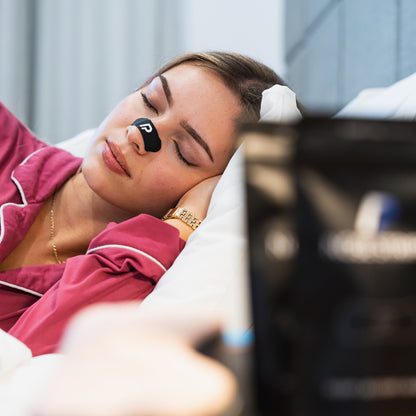 Close-up of woman sleeping with a black nasal strip for night-time airflow support